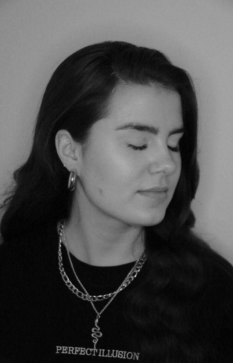 Porträt von LIIVIA mit geschlossenen Augen und gewelltem Haar, schwarze Kleidung und Schmuck.